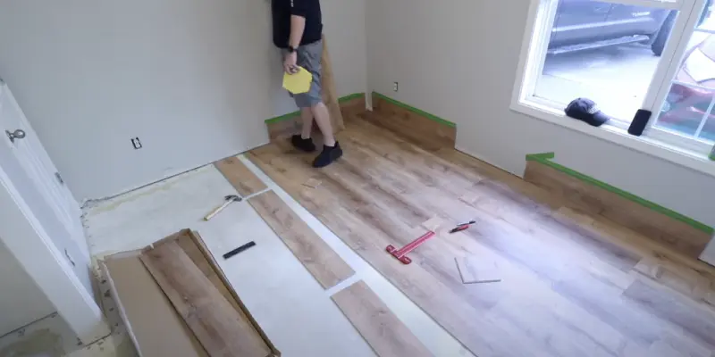 A person in a black T-Shirt and blue shorts standing in the room in which he is working on installing LifeProof flooring