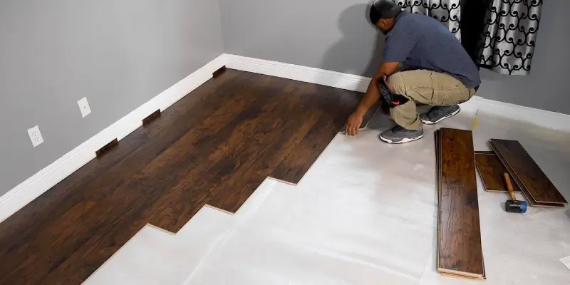 A person in a blue T-Shirt, shoe, and skin color pants installing the floor of a room
