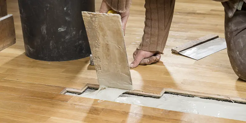 A handyman is repairing a hardwood floor of brown color