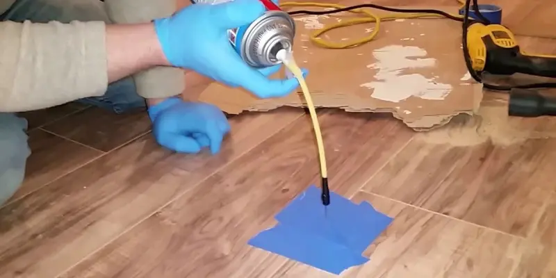 A person wearing a blue glove repairing a wood floor of laminate with the help of some product