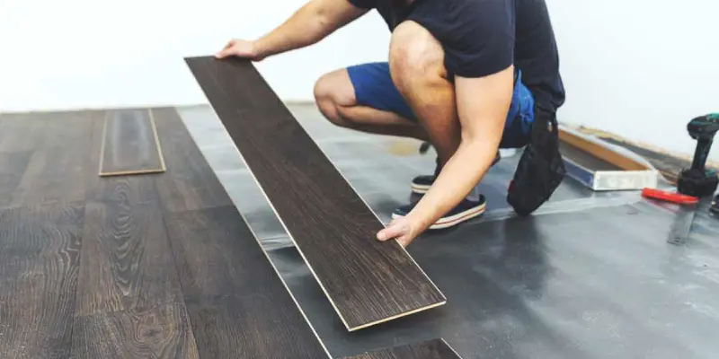 A person in a black T-Shirt and blue shorts installing vinyl flooring